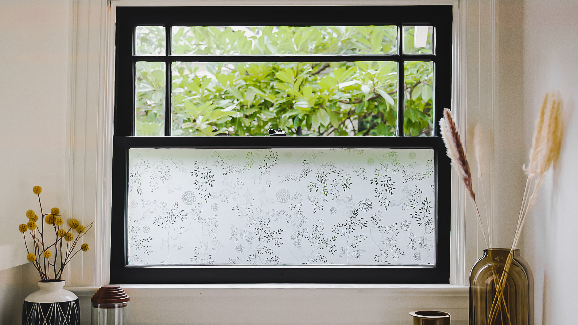 Load video: Window with window film on bottom pane and dried grasses displayed on both sides.