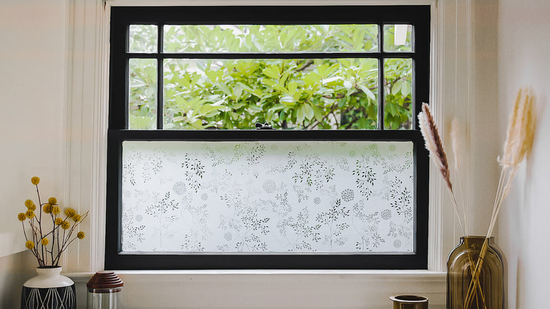 Window with window film on bottom pane and dried grasses displayed on both sides.